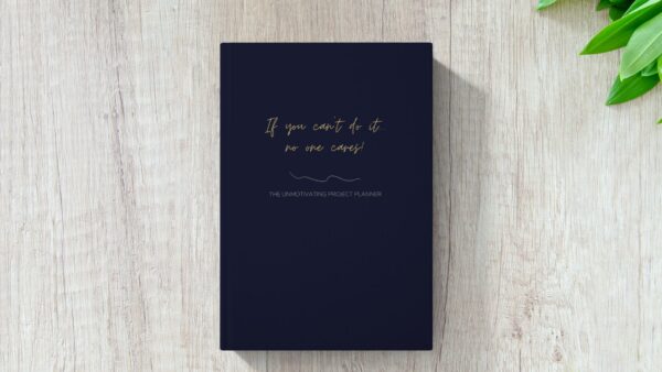 Mock up image of hardcover funny unmotivating project planner sitting on a desk. Dark blue matte cover "If you can't do it, no one cares."