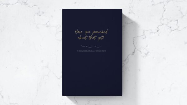 Mock up image of hardcover funny unmotivating project planner sitting on a desk. Dark blue matte cover