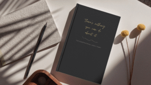 Mock up image of Undated hardcover diary sitting on a desk. Black mat cover "There's nothing you can do about it" Uninspirational Weekly Diary