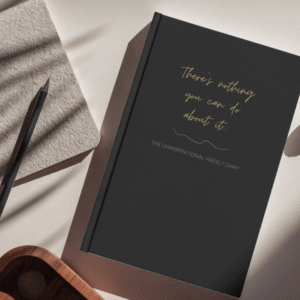 Mock up image of Undated hardcover diary sitting on a desk. Black mat cover "There's nothing you can do about it" Uninspirational Weekly Diary