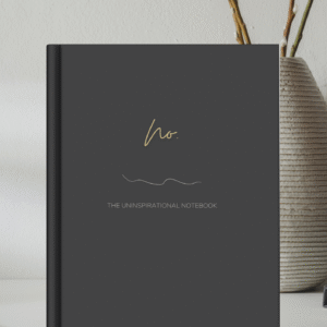 Mock up image of sleek hardcover notebook journal sitting on a desk. Black matte cover "No." Uninspirational notebook