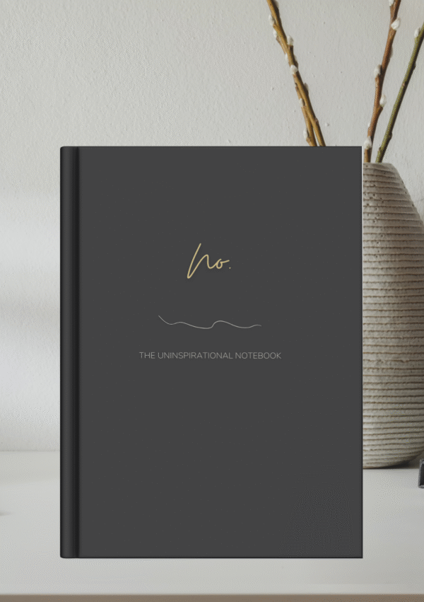 Mock up image of sleek hardcover notebook journal sitting on a desk. Black matte cover "No." Uninspirational notebook