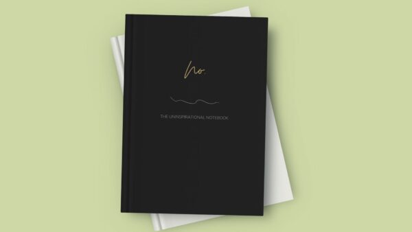 Mock up image of sleek hardcover notebook journal sitting on a desk. Black matte cover "No." Uninspirational notebook